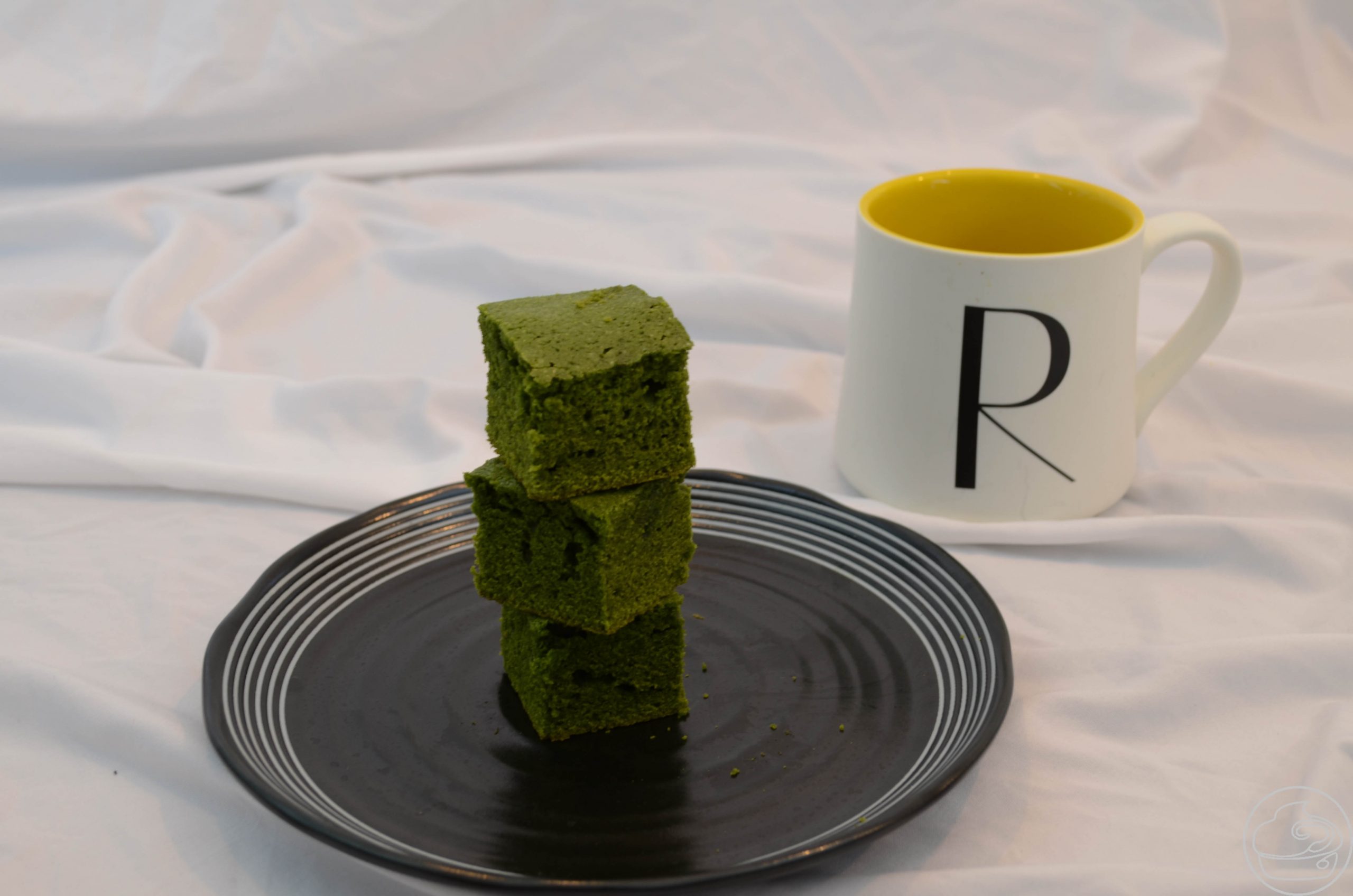 Matcha Bites stacked on a black plate on a white tablecloth with a yellow and white cup