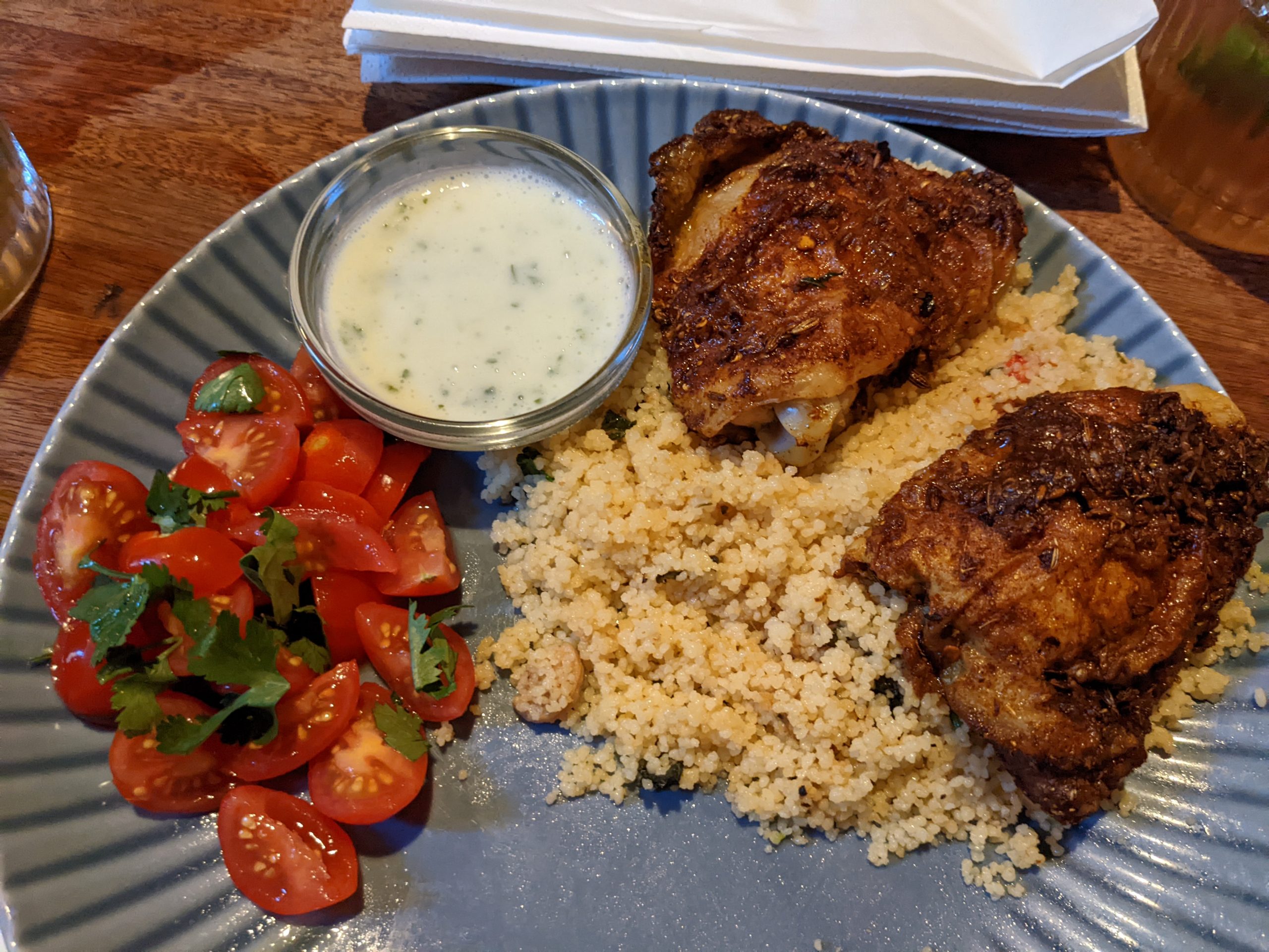A blue plate with tomatoes, couscous, and grilled chicken