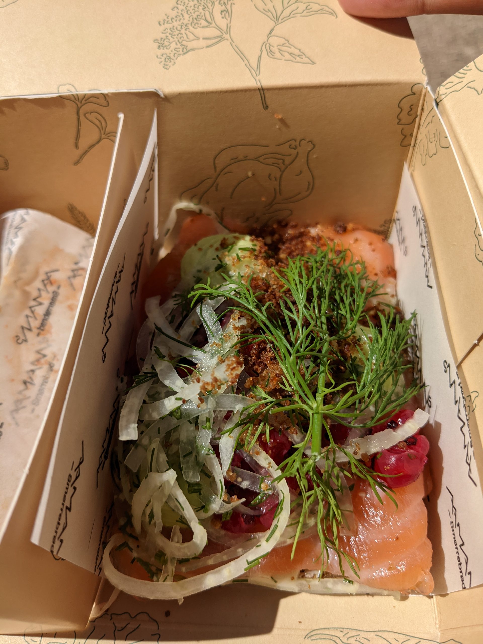 A box holding smoked salmon, with onions,, dill and lingonberries on top