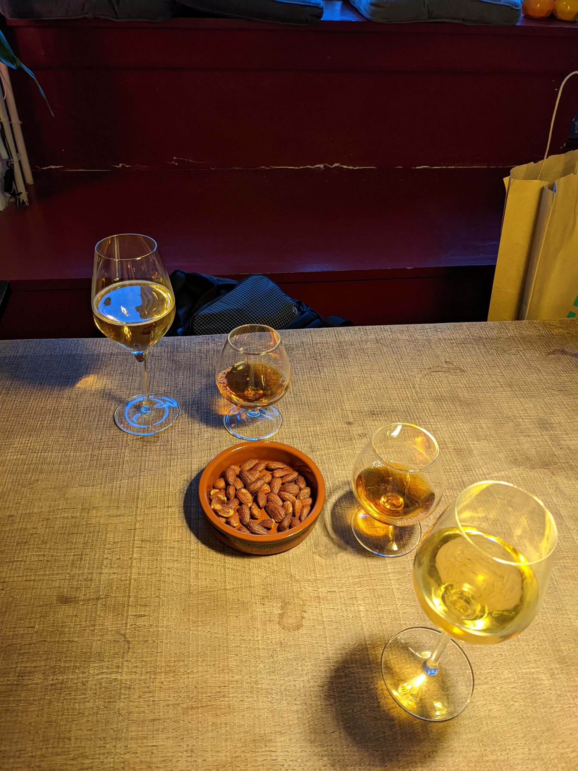 Two glasses of cider in wine glasses with two smaller glasses of alcohol and a plate of peanuts sits in between the glasses on a table