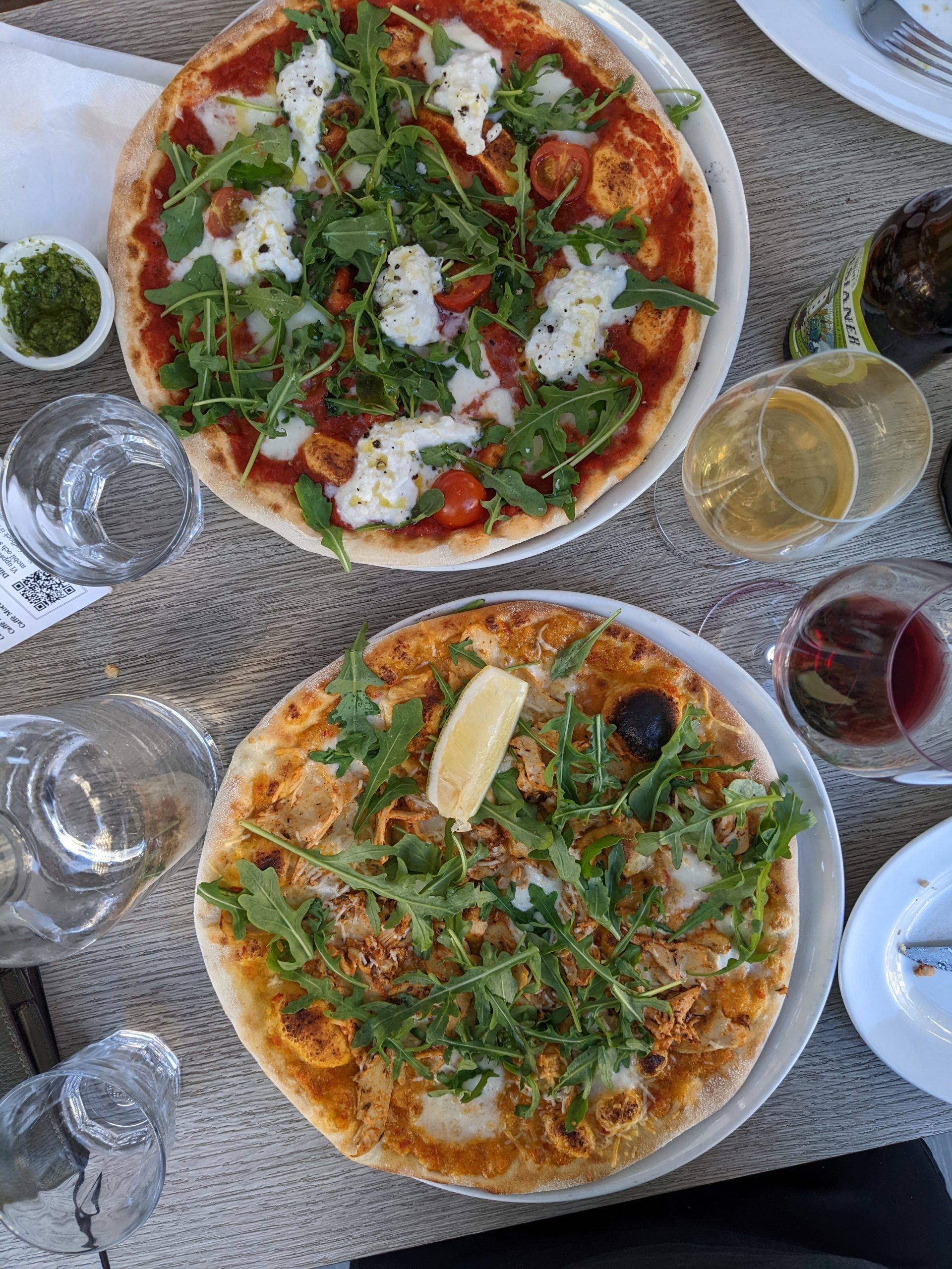 Two pizzas on top of a table surrounded by drinks