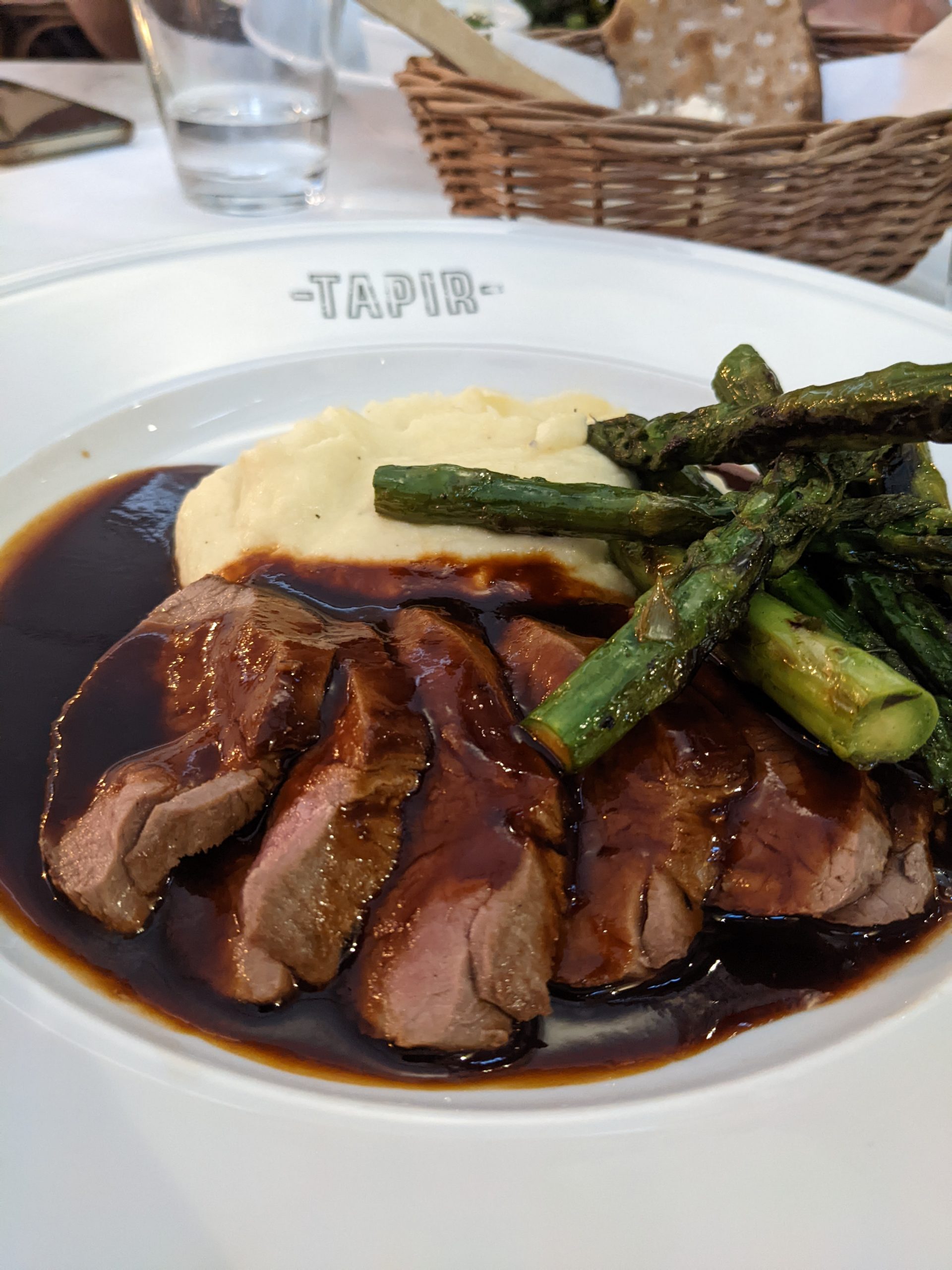A plate with slices of meat in gravy with mashed potatoes and asparagus