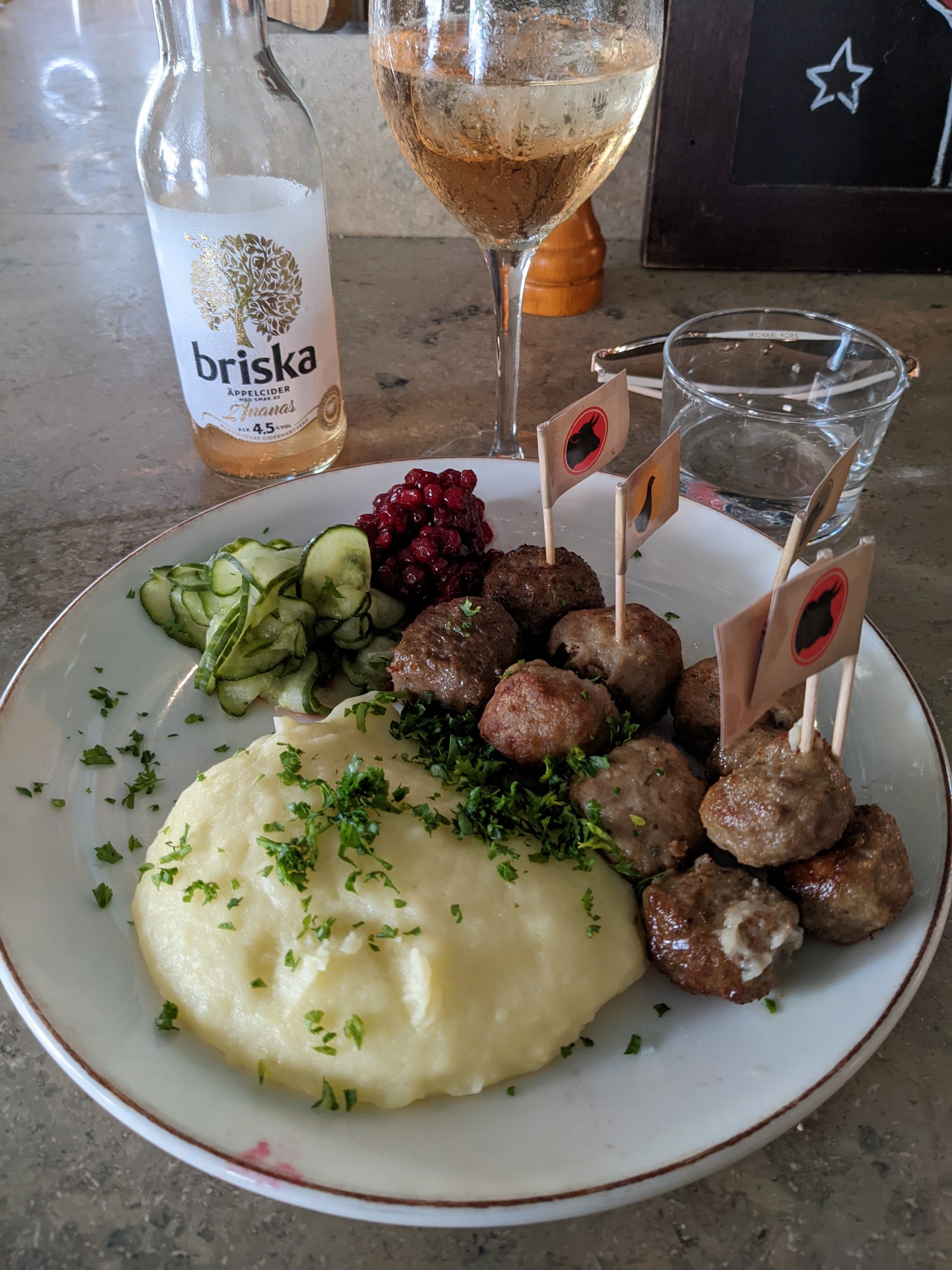 A plate with meatballs and mashed potatoes, beside it is a glass and a bottle.