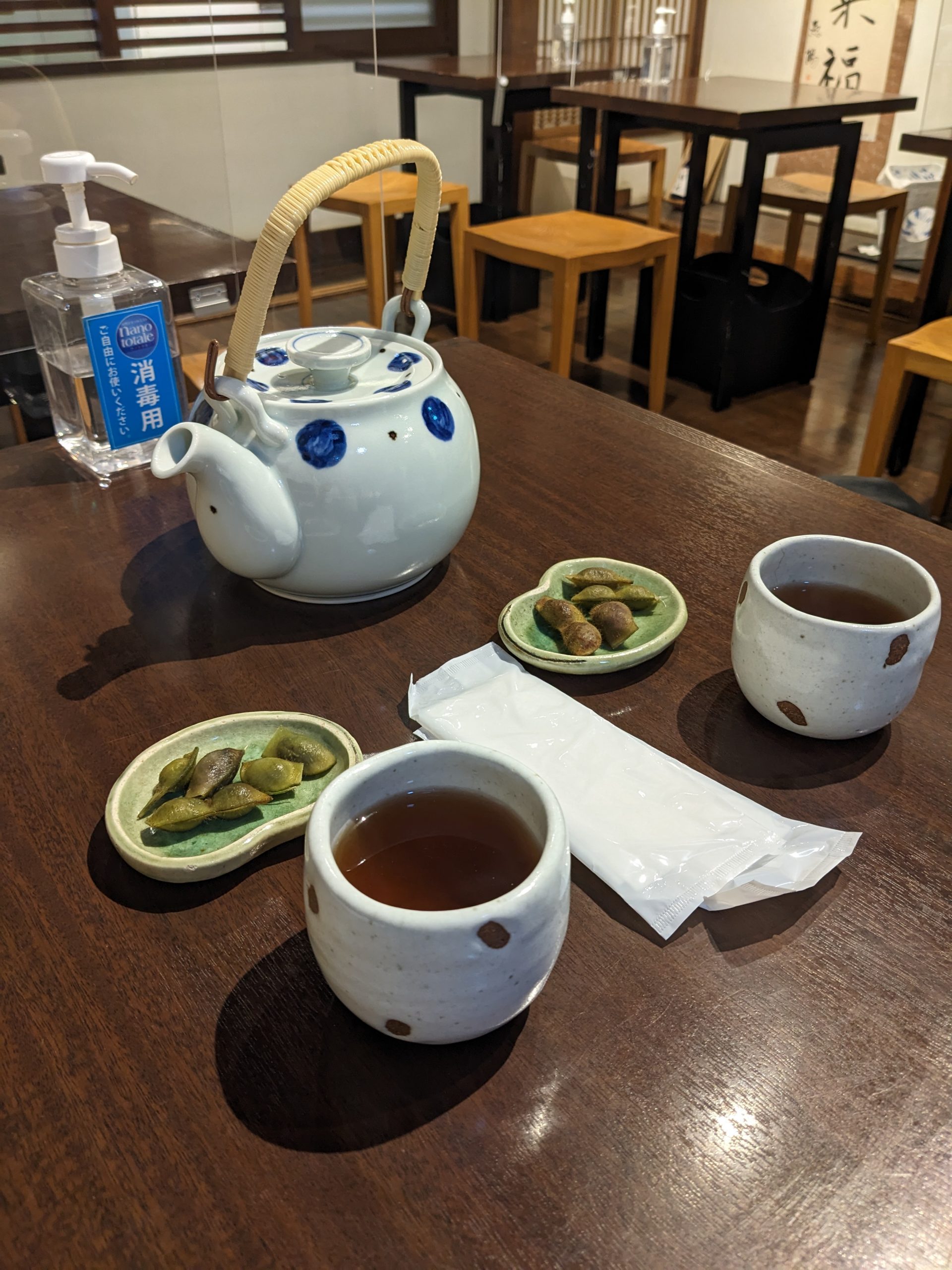 Two white tea cups filled with tea sit across from each other. Two small green dishes filled with beans are next to the cups and a teapot.
