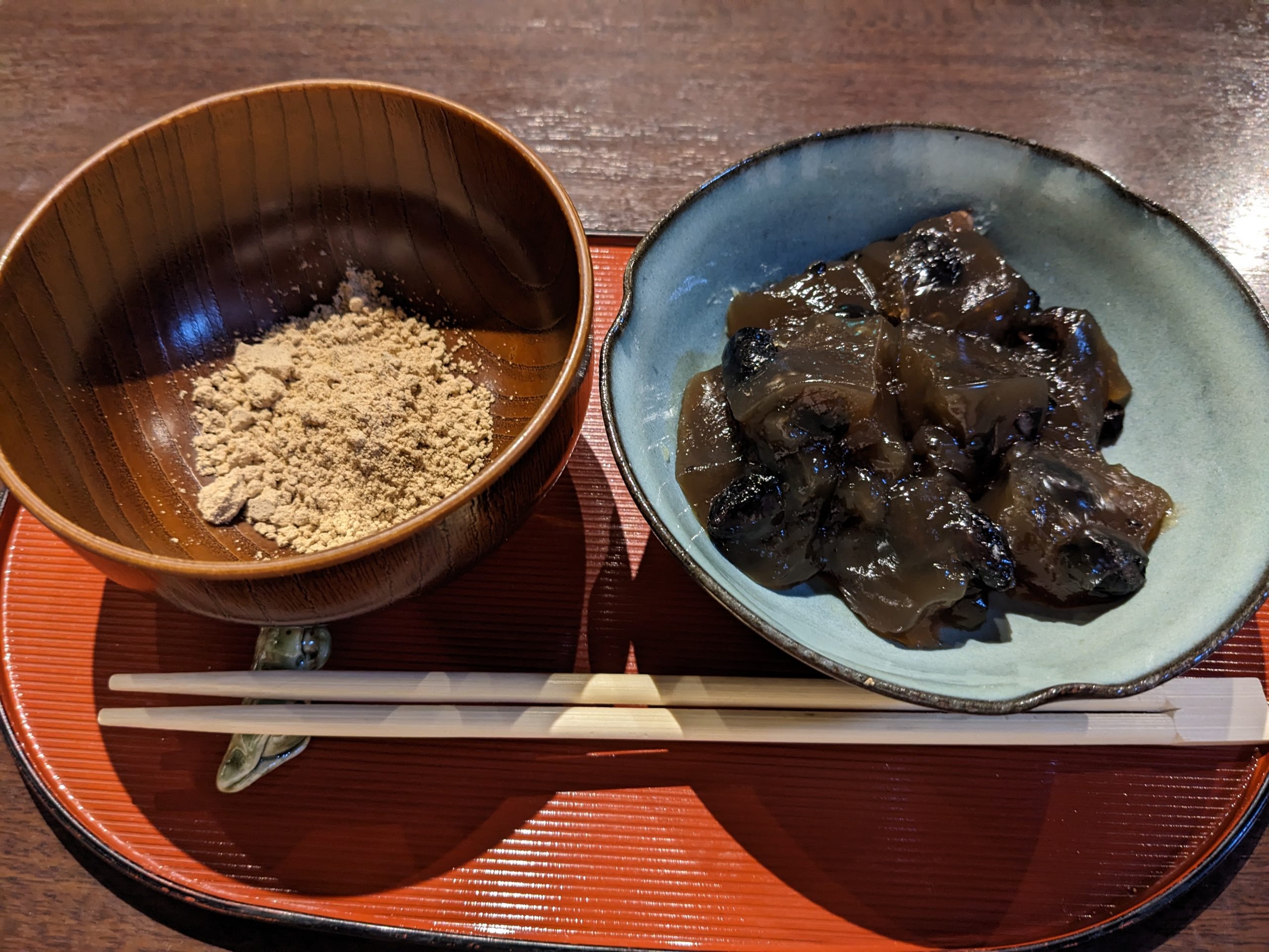 Warabi mochi in a blue bowl. Next to the blue bowl is another bowl filled with kinoko powder.