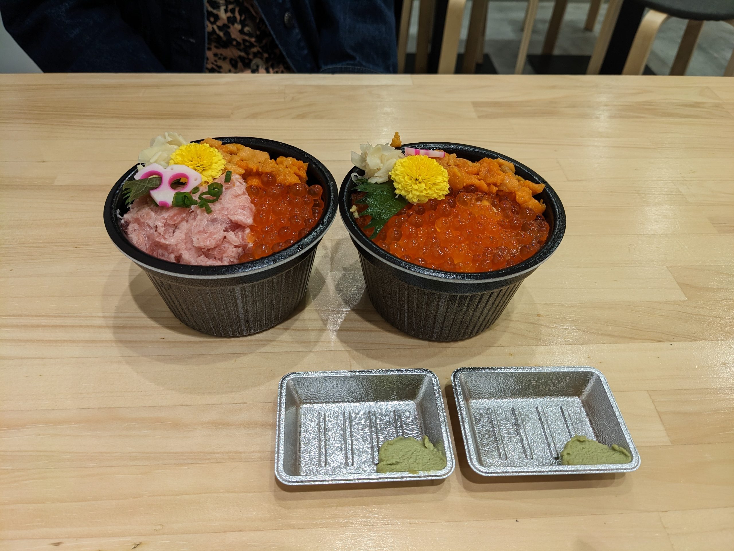 Two small bowls of raw seafood rice with two small metal dishes with wasabi in one corner