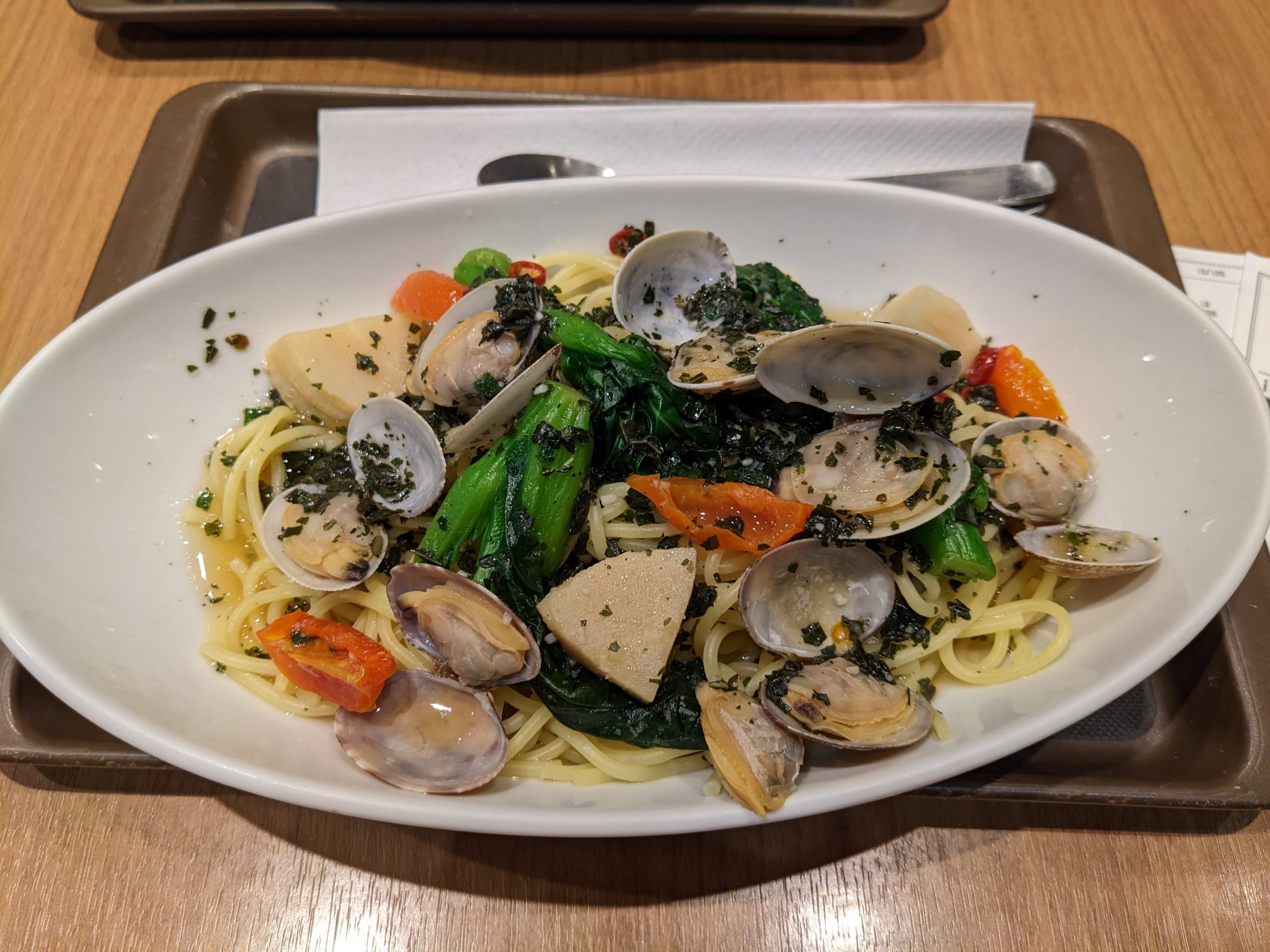 A plate of pasta with vegetables and clams in a white bowl